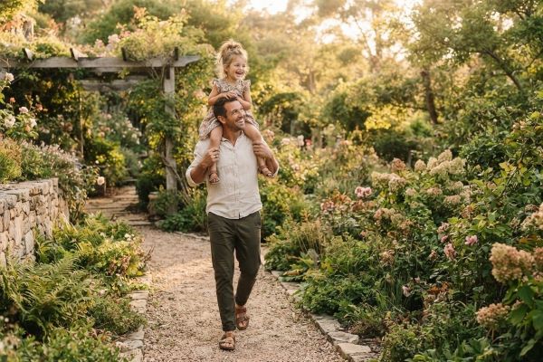 A man walking through a garden carrying a young child on his shoulders